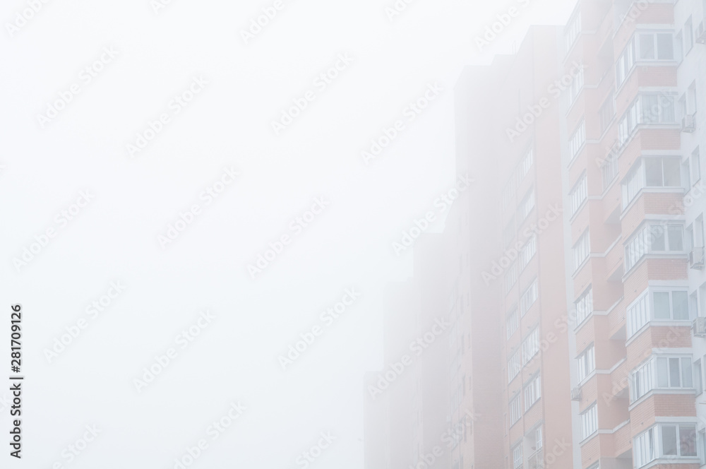 Red brick multi-storey building in the dense fog. High-Rise residential house in the milky morning fog. Free space for text. Concept for the sale of apartments in multi-storey buildings.