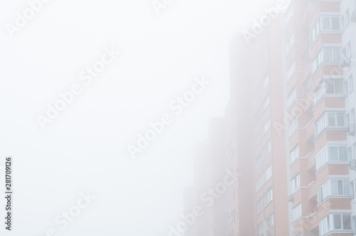 Red brick multi-storey building in the dense fog. High-Rise residential house in the milky morning fog. Free space for text. Concept for the sale of apartments in multi-storey buildings.
