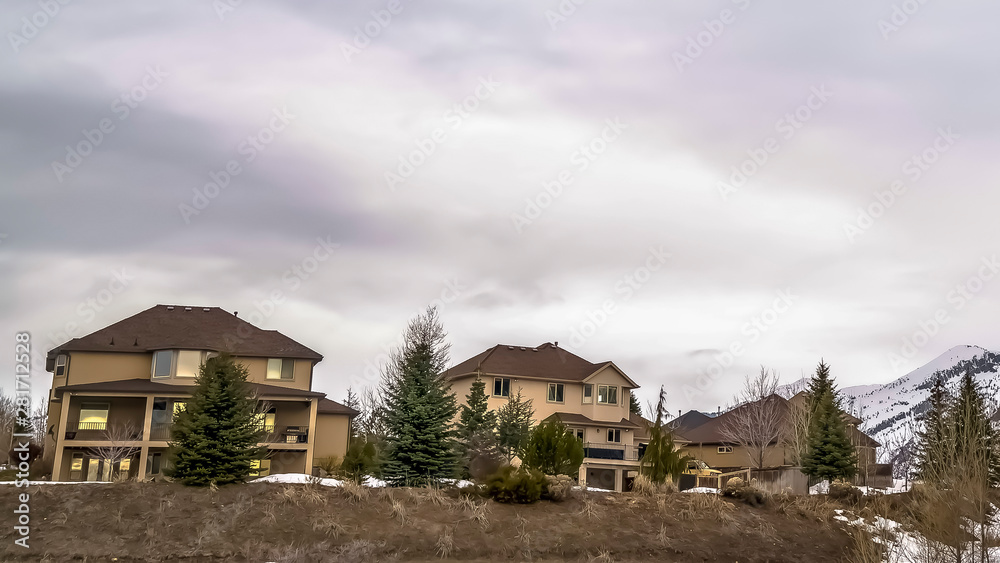 Panorama Vast cloudy sky over residential area built on snowy hill with coniferous trees