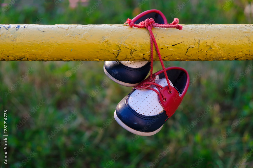 Pair of children's colored shoes with red laces hanging on a yellow pipe. The first leather shoes.