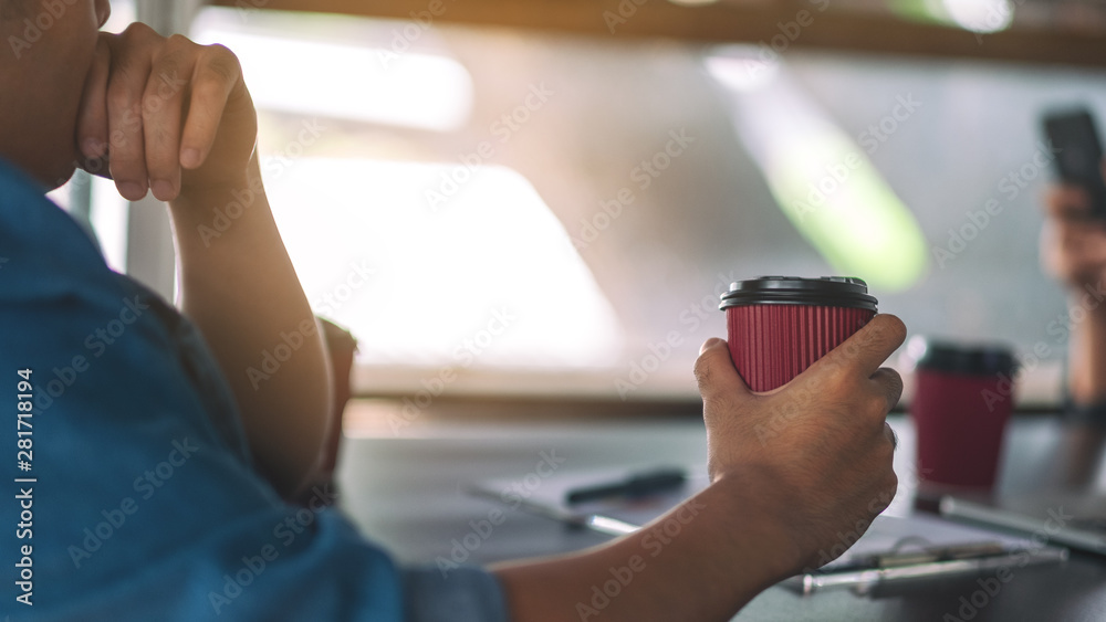 A businessman holding a paper coffee cup to drink while working in a meeting A businessman holding a paper coffee cup to drink while working in a meeting