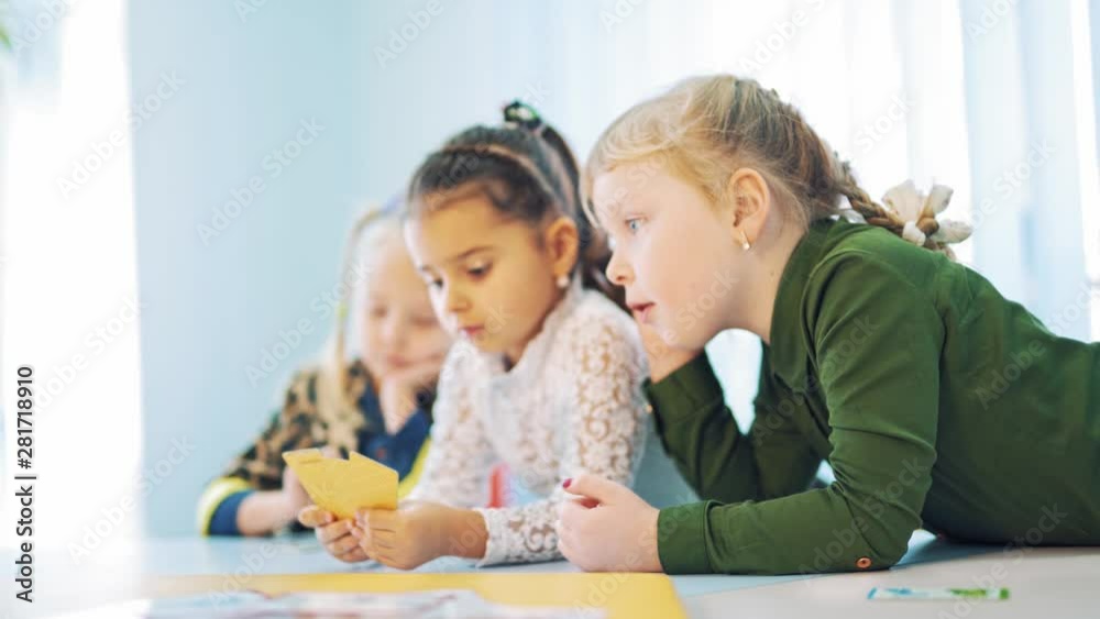 Curious girls at the table at school. Three mobile kids leaning on the table during the lesson. Elementary school. Close-up. Curious girls at the table at school. Three mobile kids leaning on the table during the lesson. Elementary school. Close-up.