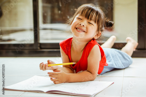 Little girl drawing with colorful crayons and smiling, in colorful room.