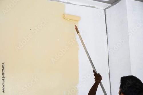 Back view of Thai young painter use paint roller applying color on wall of new building house.