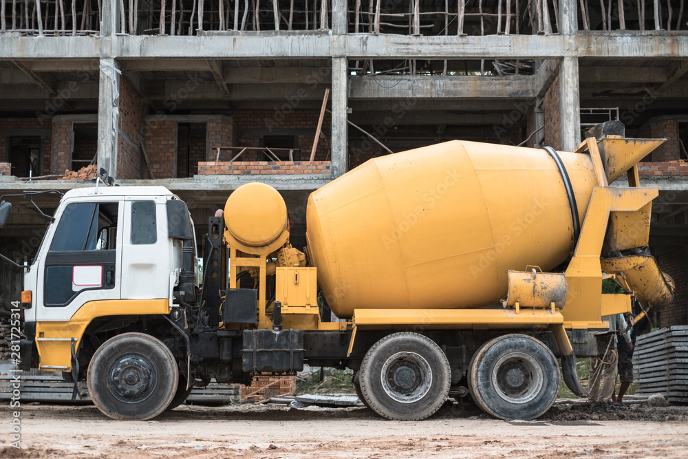 Old yellow cement mixer truck in front of building under construction. Construction machinery. Old yellow cement mixer truck in front of building under construction. Construction machinery.