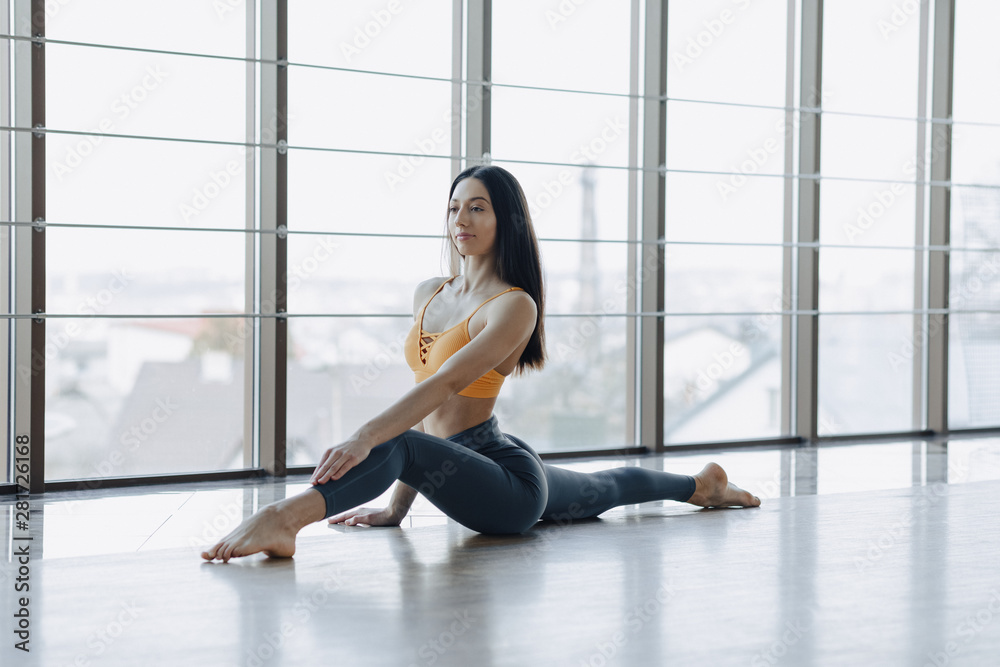 young attractive girl doing fitness exercises with yoga on the floor against the background of panoramic windows