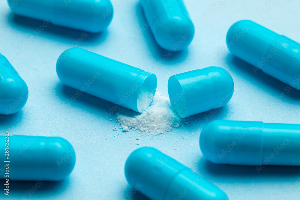 Blue tablets in capsules. One capsule is open. Blue background Blue tablets in capsules. One capsule is open. Blue background