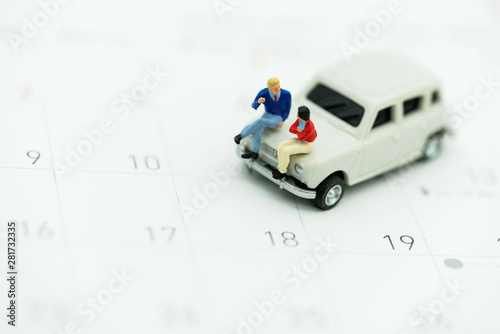 Miniature people sitting on car with calendar.