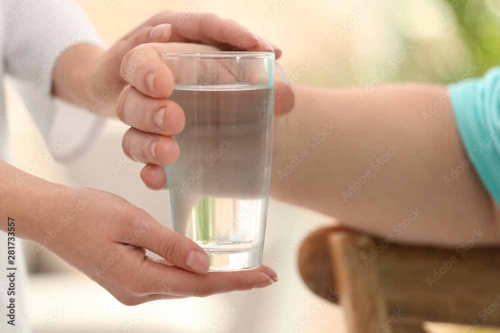 Nurse giving glass of water to elderly man indoors, closeup. Assisting senior generation Nurse giving glass of water to elderly man indoors, closeup. Assisting senior generation