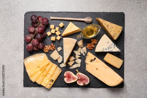 Slate board with different types of delicious cheese and snacks on grey table, top view photo