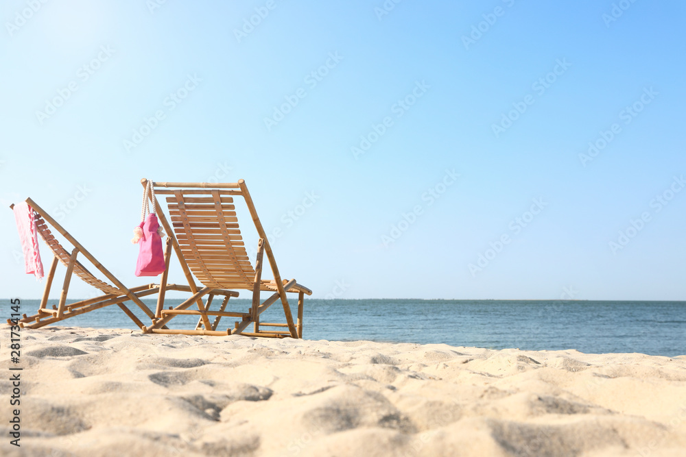 Empty wooden sunbeds and beach accessories on sandy shore