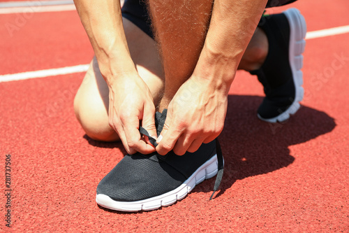 Man tying shoelaces on red athletic running track, close up