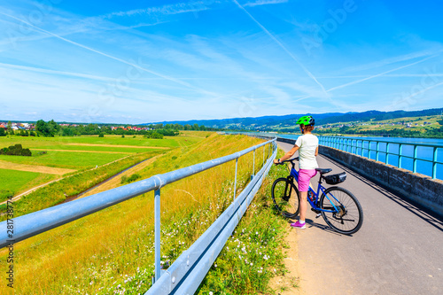 Young woman cyclist standing on cycling way along Czorsztynskie lake in Frydman village, Pieniny Mountains, Poland photo