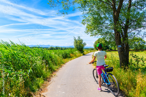 Young woman riding bike on cycling way along green fields near Czorsztynskie lake and Nowy Targ, Tatra Mountains, Poland
