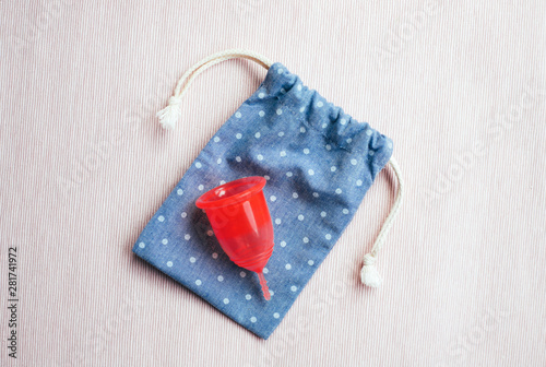 Red menstrual cup on cotton bag on pink background.
