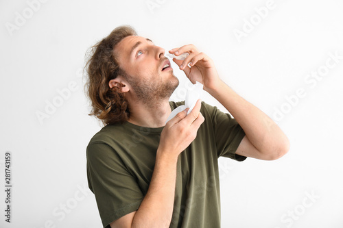 Young man with nasal drops and tissue on light background