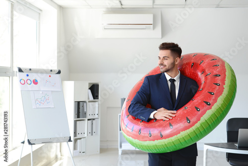 Handsome businessman with inflatable ring in office. Travel concept