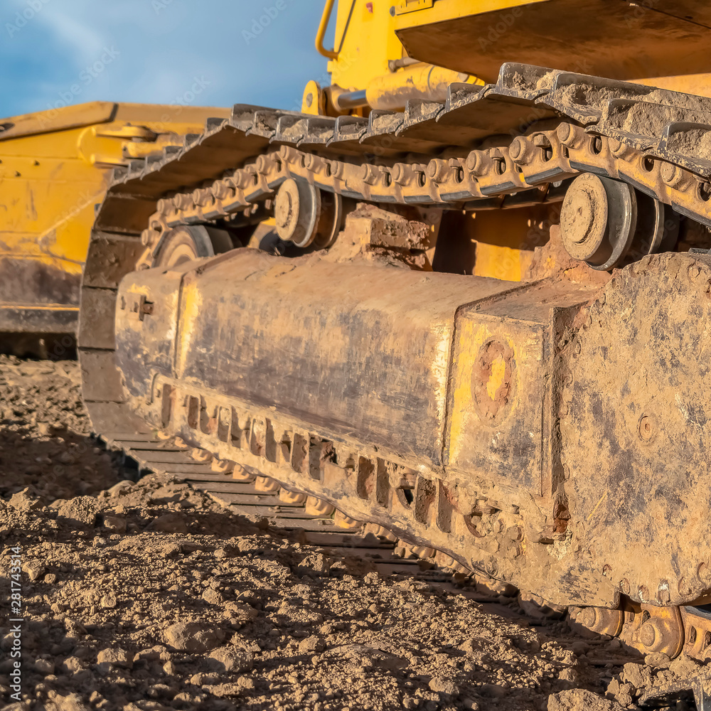 Square Yellow excavator with close up view of the grouser pad track frame and rollers