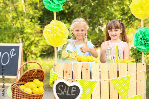 Cute little children selling lemonade in park