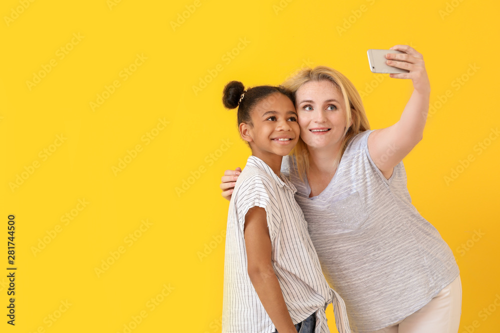 Happy woman with her African-American daughter taking selfie on color background - obrazy, fototapety, plakaty 
