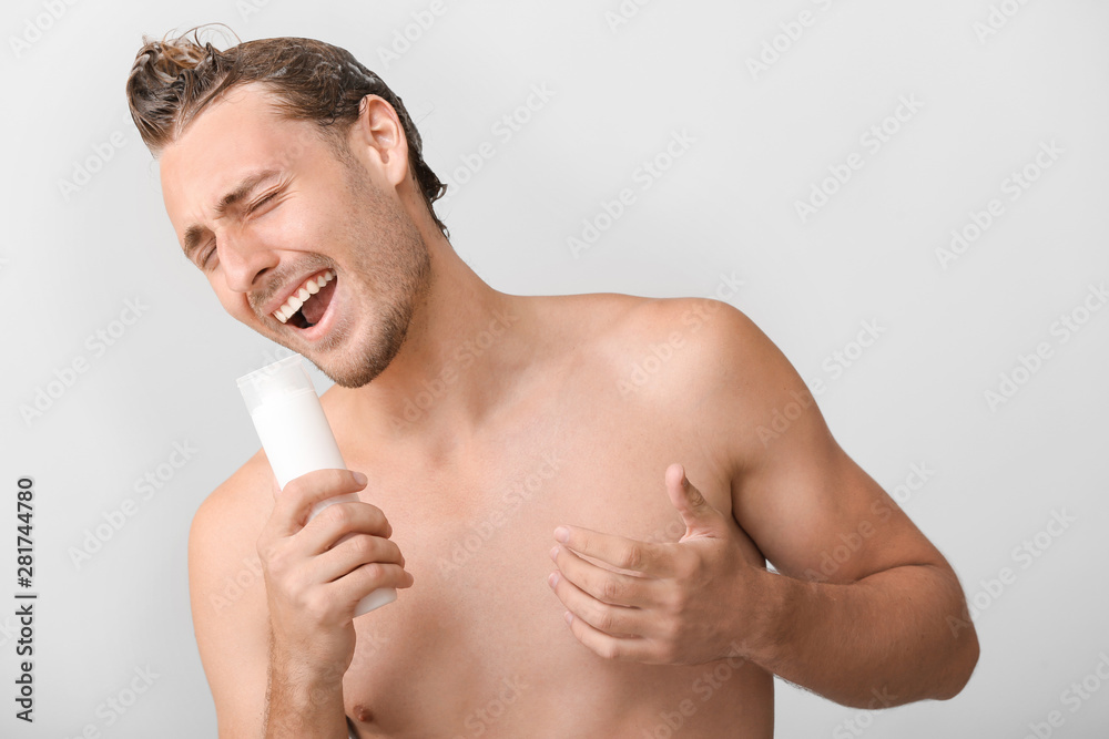 Fototapeta premium Handsome young man using bottle of shampoo as microphone against grey background