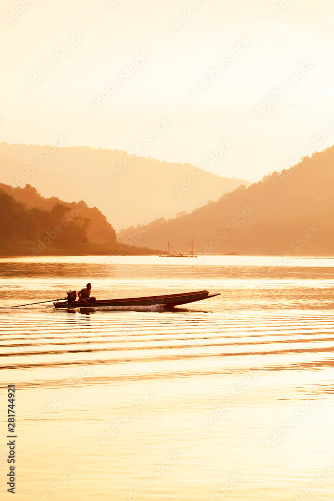 Male fisherman steering wooden fishing boat on the lake at dusk.