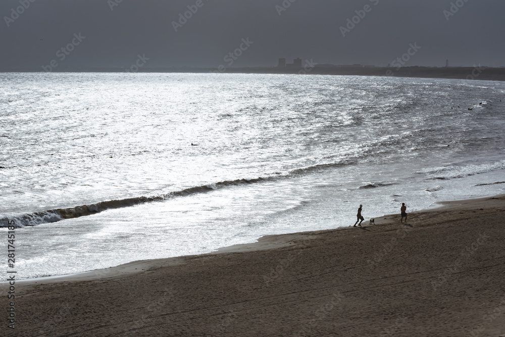 pedestrian on the beach with sparkling reflection of sunlight on the sea surface