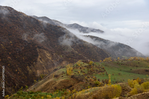 Mountains shrouded in mist in the season of golden autumn on a cloudy day, view of the gorge from the top of the mountain. © StockAleksey