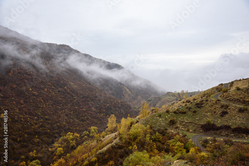Mountains shrouded in mist in the season of golden autumn on a cloudy day, view of the gorge from the top of the mountain.