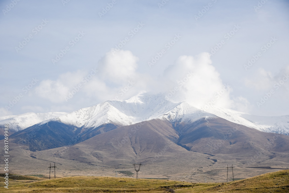snow-capped peaks of mountains in the background, on a bright sunny day with clouds on the sky covered with golden, yellow autumn grass.