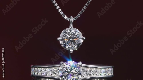 View of a beautiful platinum ring and pendant with diamonds, against a burgundy background.