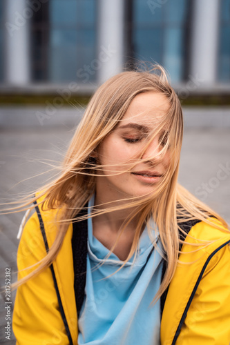 Beautiful young blonde woman on the street, posing with wind in her hair