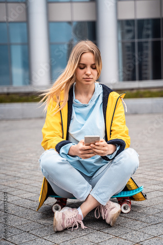 Beautiful girl uses smartphone and sits on skateboard.
