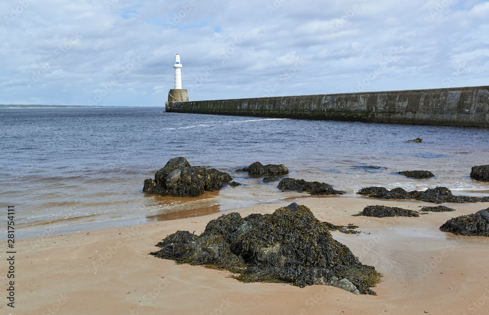 Seaweed covered rocks on Torry Beach in Aberdeen, with the harbour Breakwater and navigational light in the background.