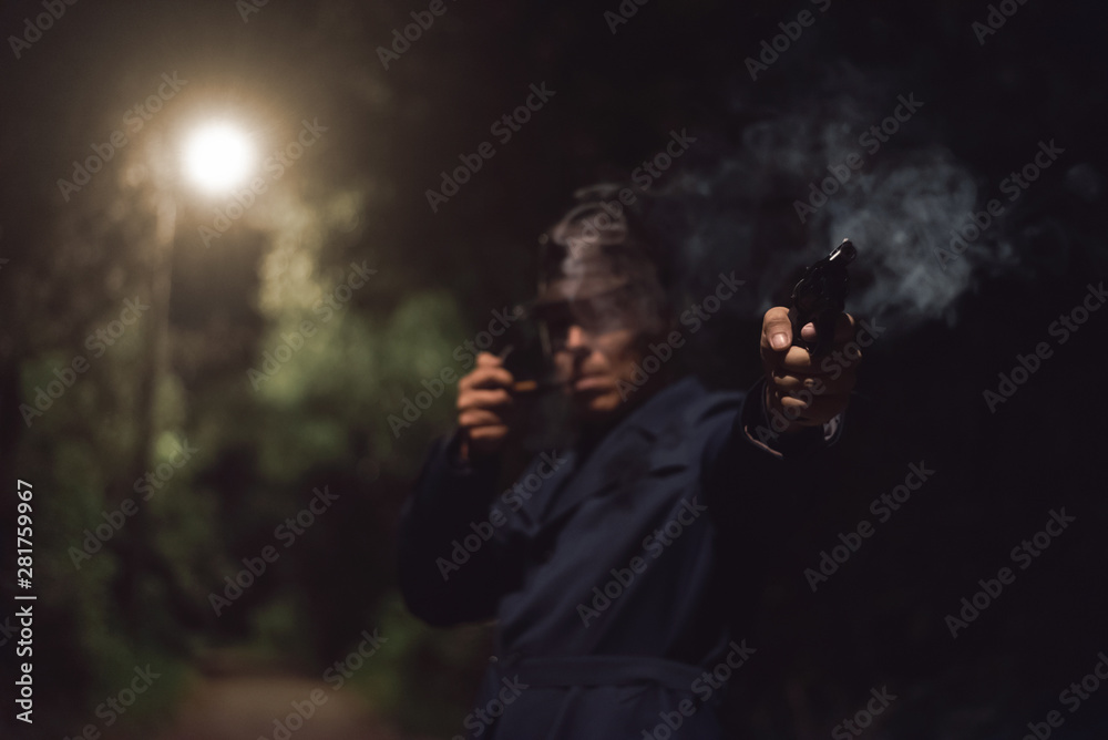 Detective agent in a hat and coat is aiming by a gun into a dark and smokes his smoking pipe. Detective agent in a hat and coat is aiming by a gun into a dark and smokes his smoking pipe.