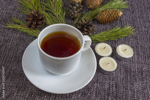 Cup of fragrant hot tea among Christmas tree branches and pine cones on a plaid.