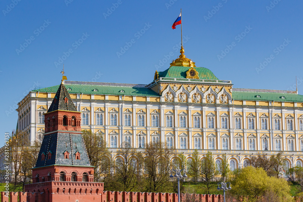Naklejka premium View of Grand Kremlin Palace with waving Russian Federation flag against tower of Moscow Kremlin on a blue sky background