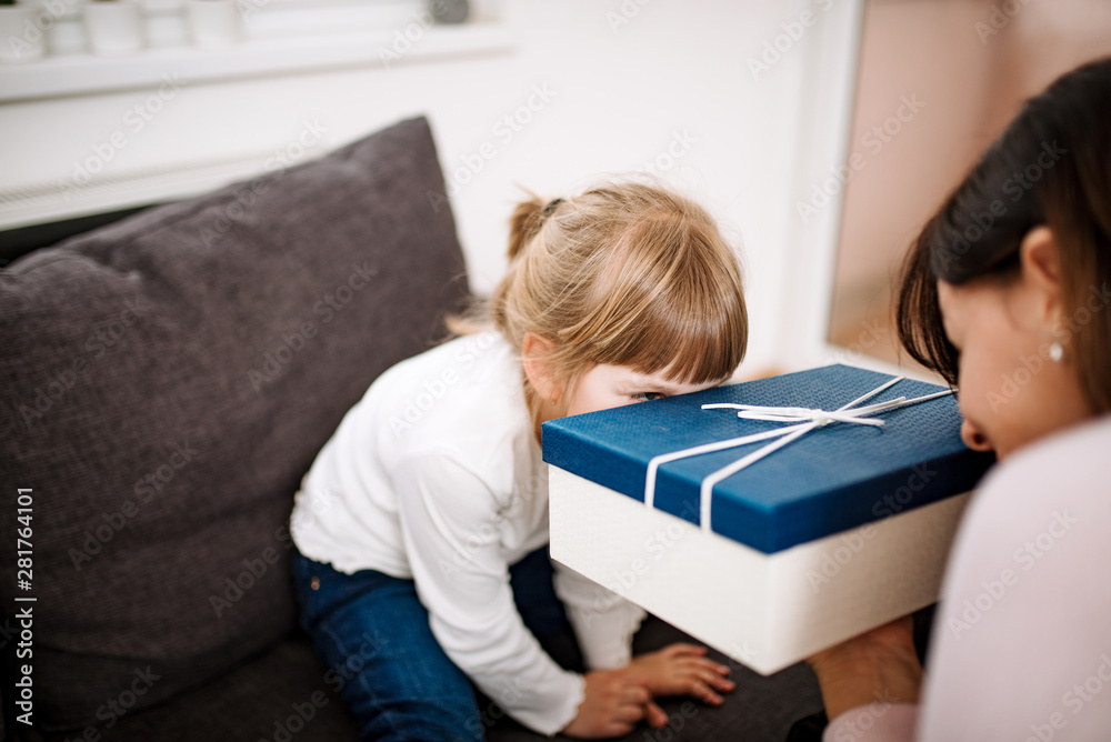 Cute little girl and her beautiful mother peeking at gift box.