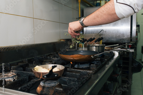 Hand of a chef adding herbs to a meal on a stove.