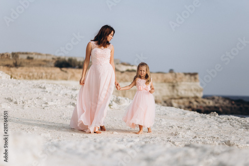 Mother and daughter on a cliff and look at the sea in pink dresses. 