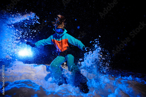 Active female snowboarder dressed in a orange and blue sportswear riding on the mountain slope