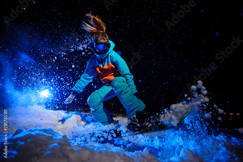 Active female snowboarder dressed in a orange and blue sportswear jumping on the snow slope © fesenko