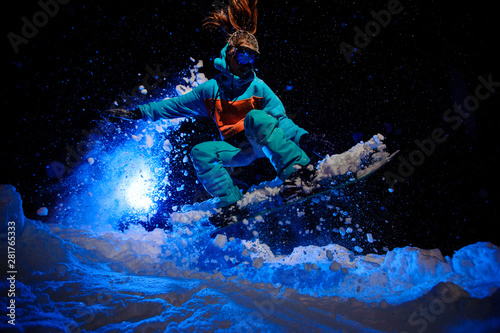 Female snowboarder dressed in a orange and blue sportswear performs tricks on the snow