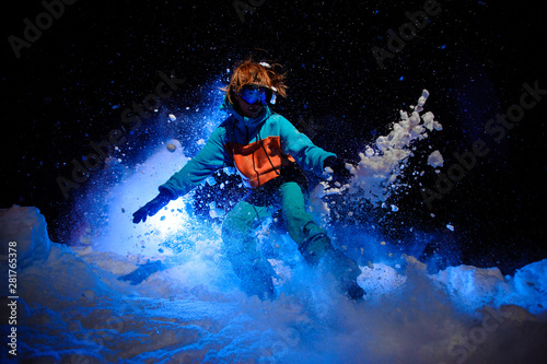 Active female snowboarder dressed in a orange and blue sportswear performing tricks on the snow
