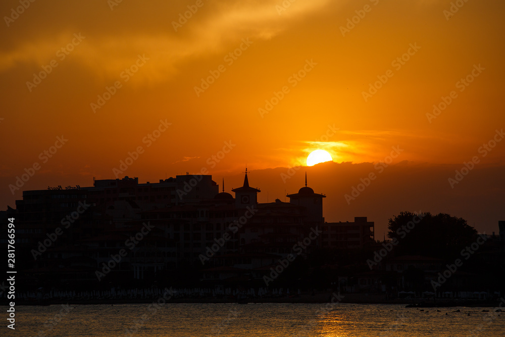 Golden sunset on the beach. Silhouette of the city. Beautiful architecort by the sea on the background of the sunset.