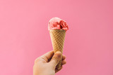 The girl holds ice cream in her hand in a cup on a pink background.