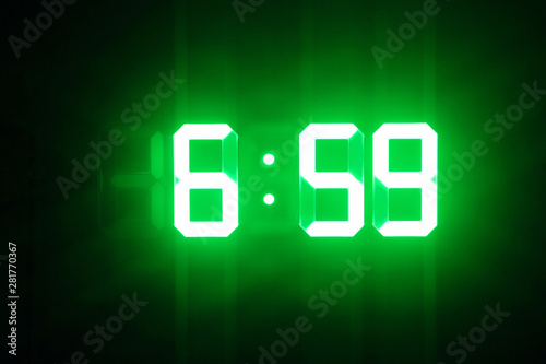 Green glowing digital clocks in the dark show 6:59 time photo