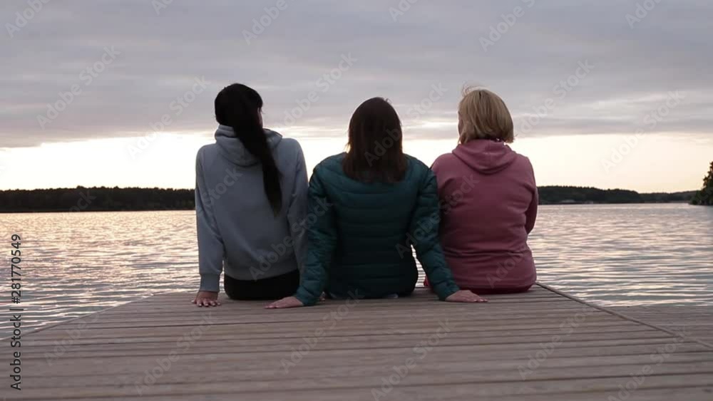 Three girls admire the sunset sitting on the pier Three girls admire the sunset sitting on the pier