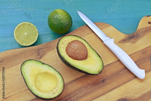 Top dish with a cut avocado, limes and a knife on wooden plate and blue background.