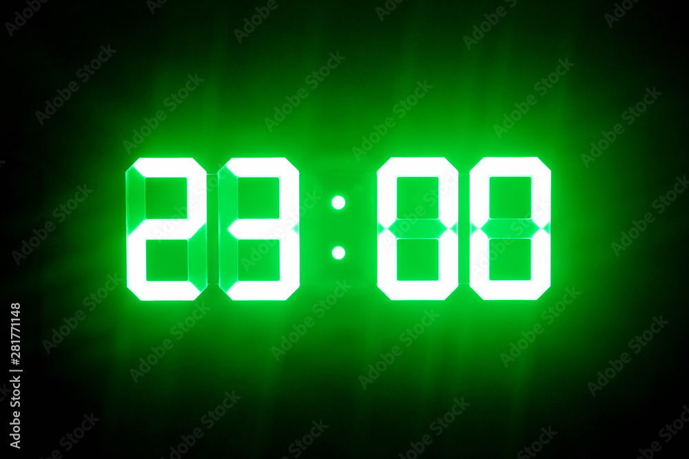 Green glowing digital clocks in the dark show 23:00 time Green glowing digital clocks in the dark show 23:00 time